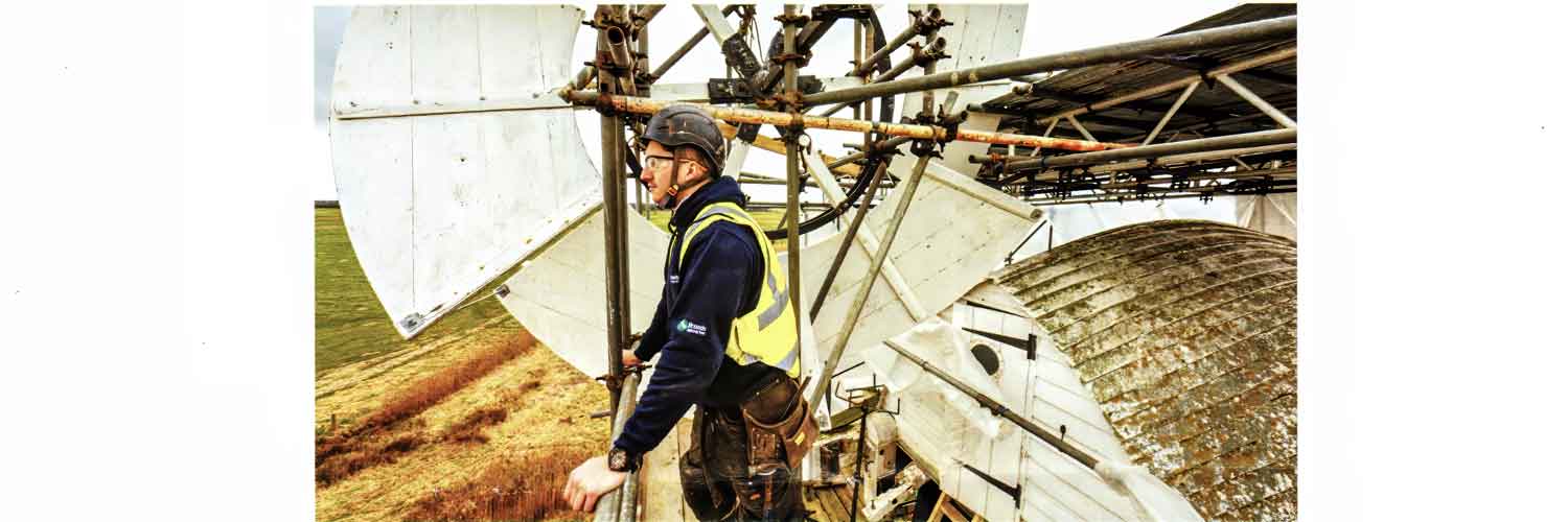  Worker om hi-viz standing on the scaffold around the mill  cap during restoration, looking out across the marsh